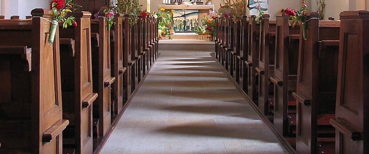 An aisle with wooden pews, floral decorations, and a central altar with statues.