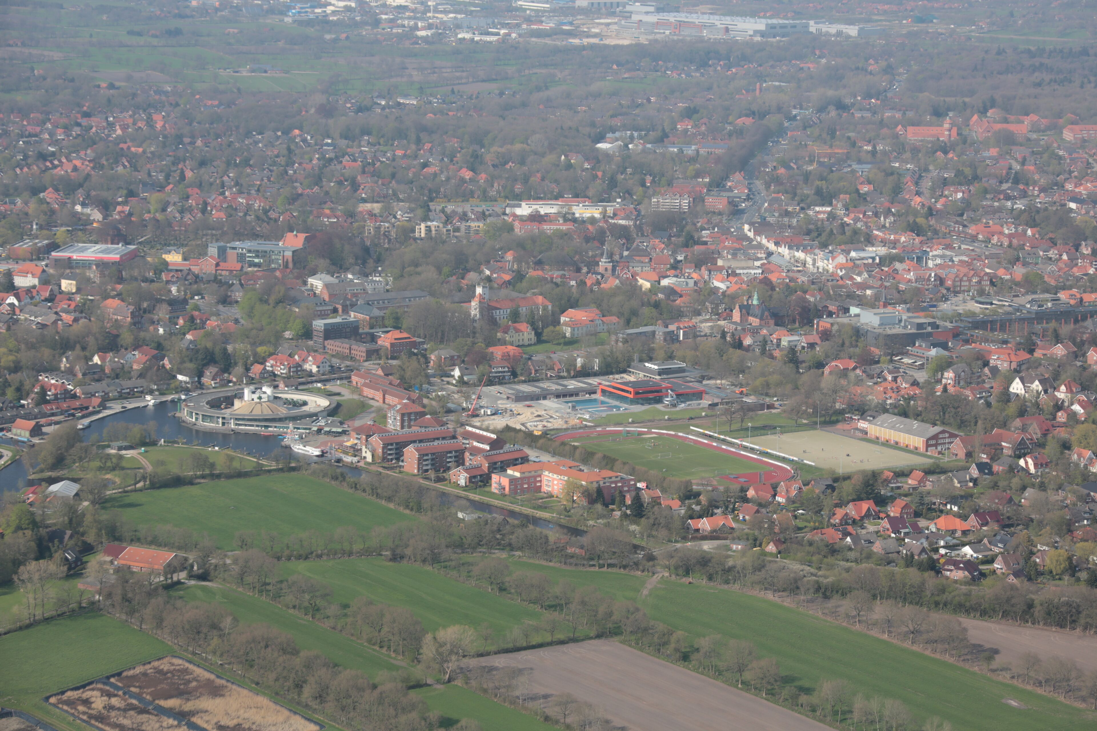 An aerial view of a town with a river, green fields, and red-roofed buildings.