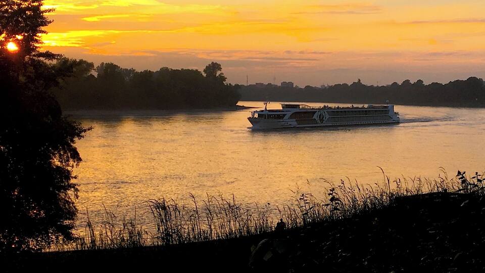 A riverboat at sunset with a city skyline in the background.