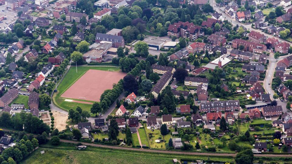Vista aérea de una zona residencial con casas, un gran campo deportivo y zonas verdes circundantes.