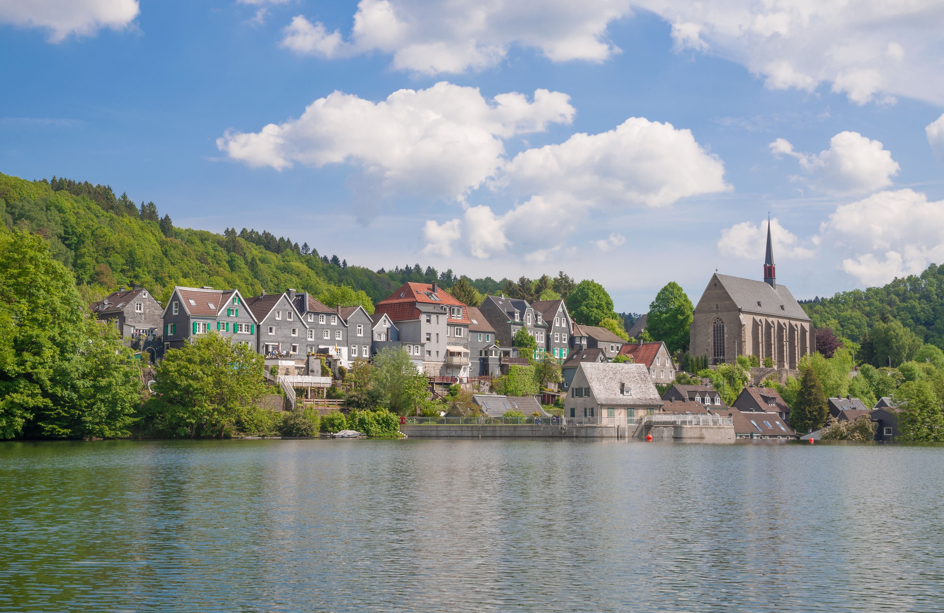 A lakeside town with colorful houses, a church, and a hill with trees.