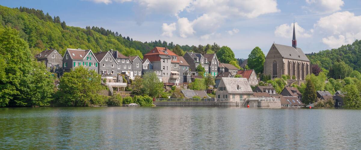 A lakeside town with colorful houses, a church, and a hill with trees.