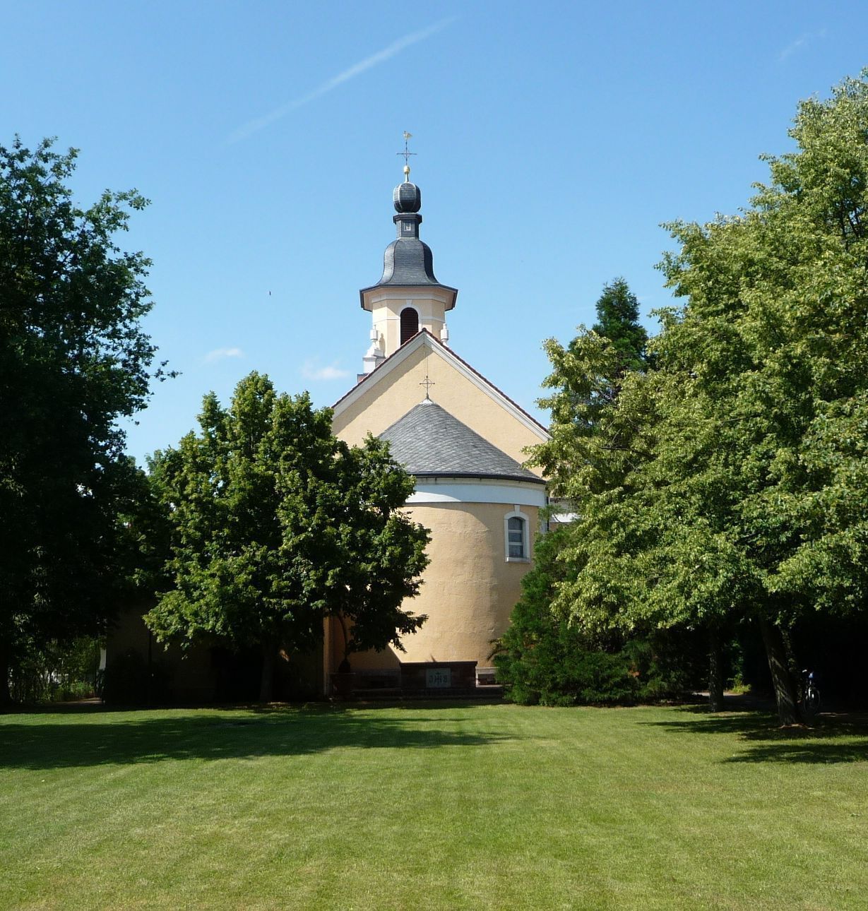 A church with a bell tower and crosses, surrounded by trees and a well-maintained lawn.