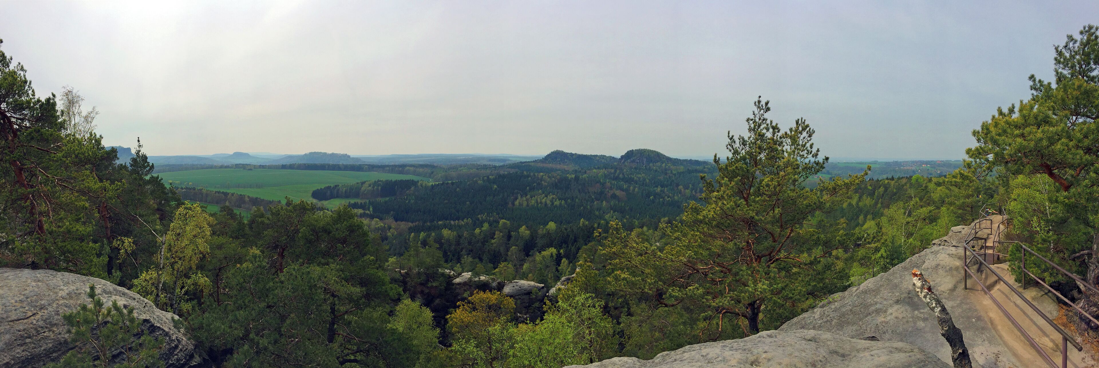 A mountainous landscape with dense forests, rocky outcrops, and a distant view of rolling hills.