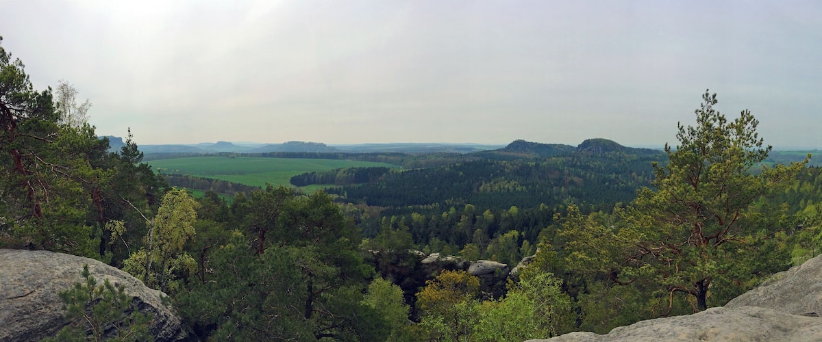 A mountainous landscape with dense forests, rocky outcrops, and a distant view of rolling hills.