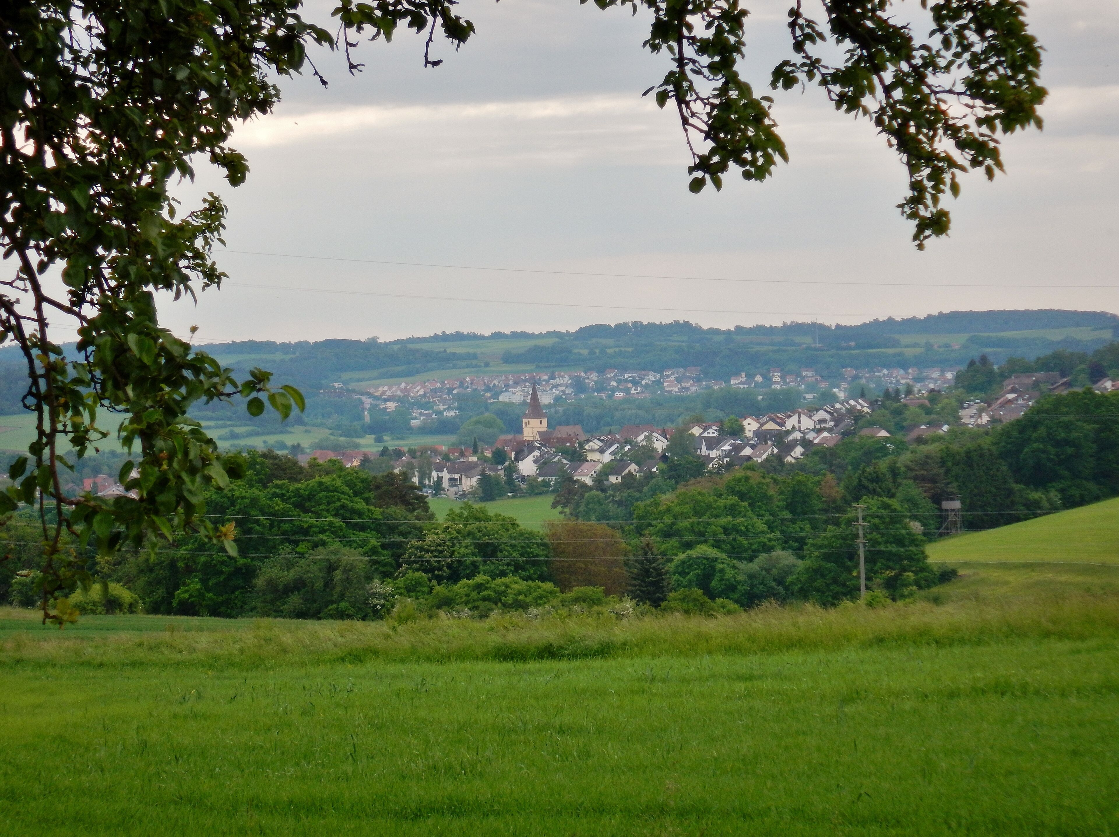 A town with a prominent church surrounded by lush green fields and rolling hills in the background.