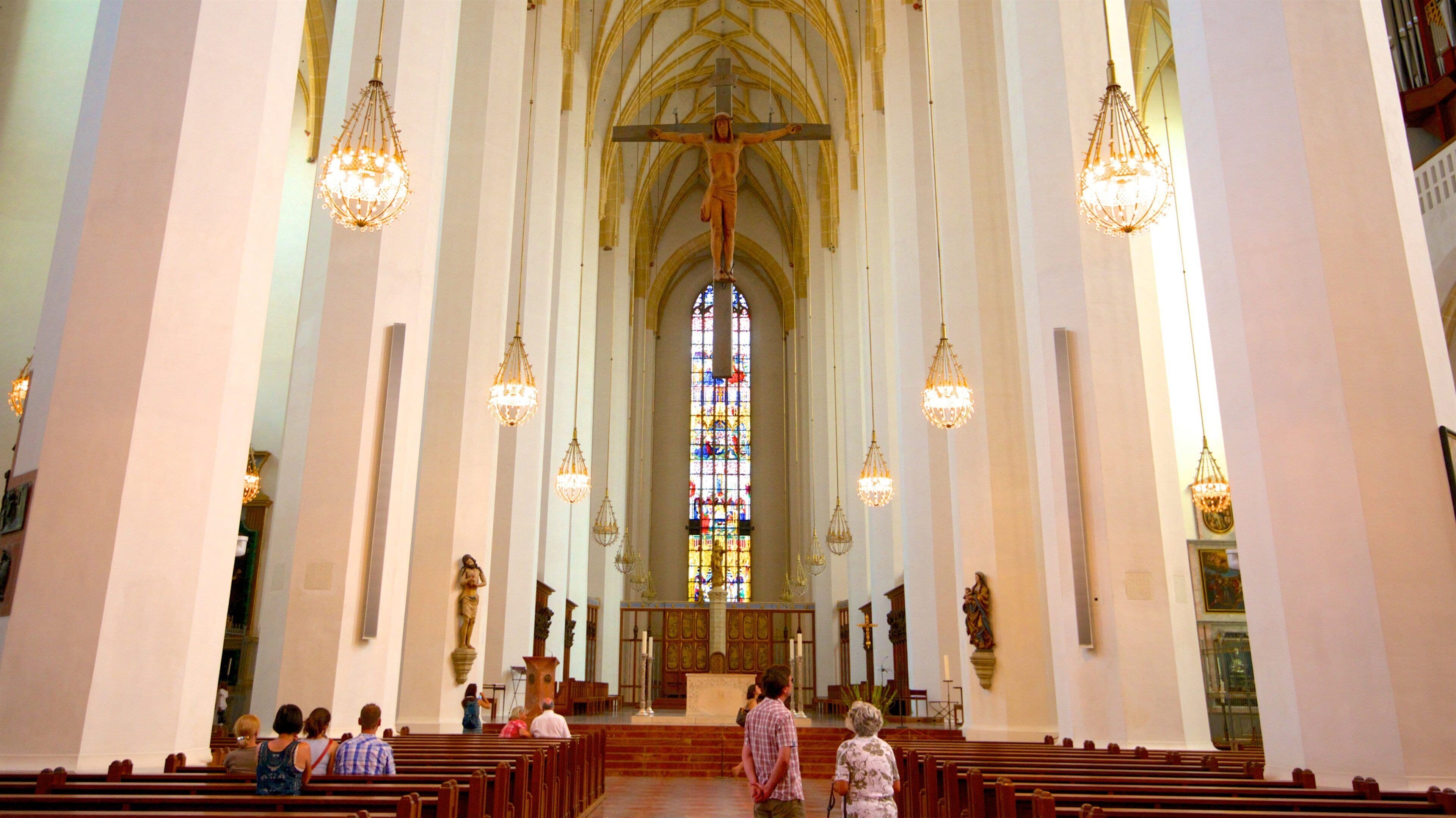 Interior de iglesia con altos techos abovedados, vidrieras de colores y bancos de madera.