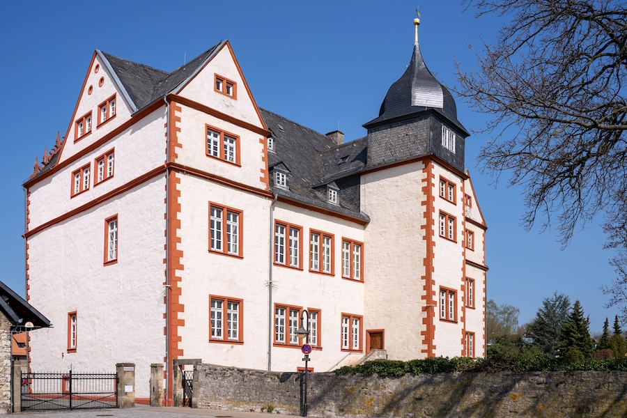 Un edificio grande e histórico con un techo pronunciado, múltiples ventanas con marcos rojos y una torre destacada con aguja.