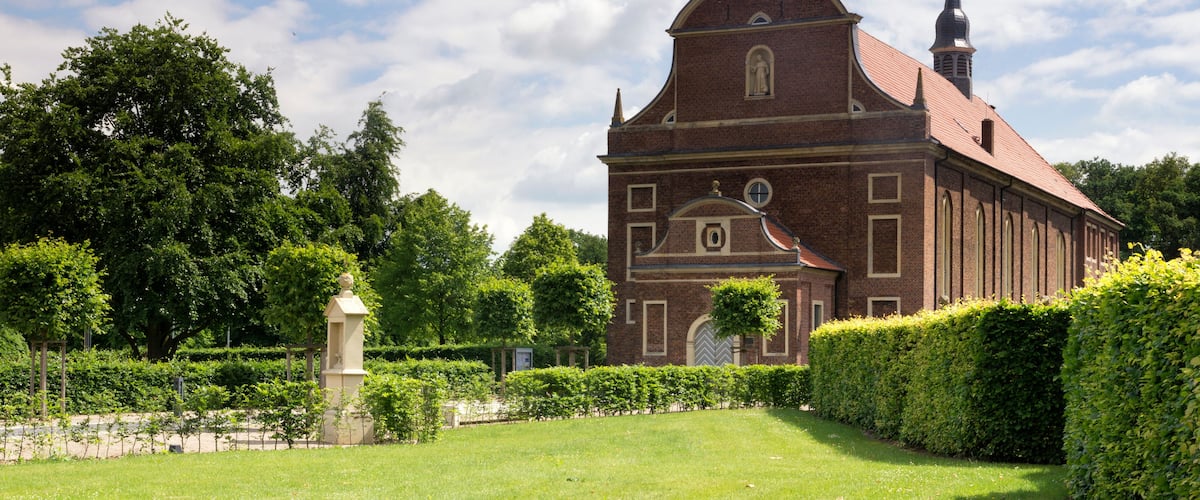 A church with a prominent steeple and a cross on top, surrounded by well-maintained hedges and a grassy lawn.