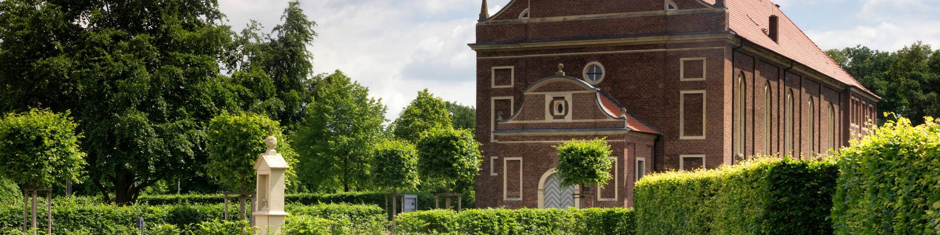 A church with a prominent steeple and a cross on top, surrounded by well-maintained hedges and a grassy lawn.
