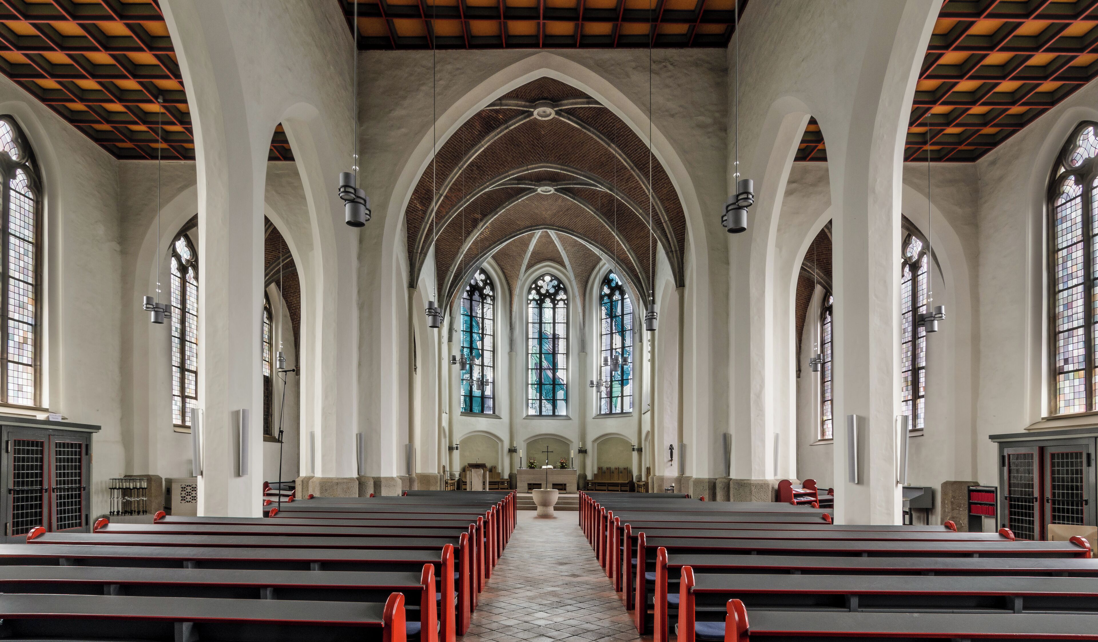A church interior with arched ceilings, stained glass windows, and rows of pews.