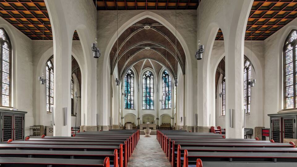 A church interior with arched ceilings, stained glass windows, and rows of pews.