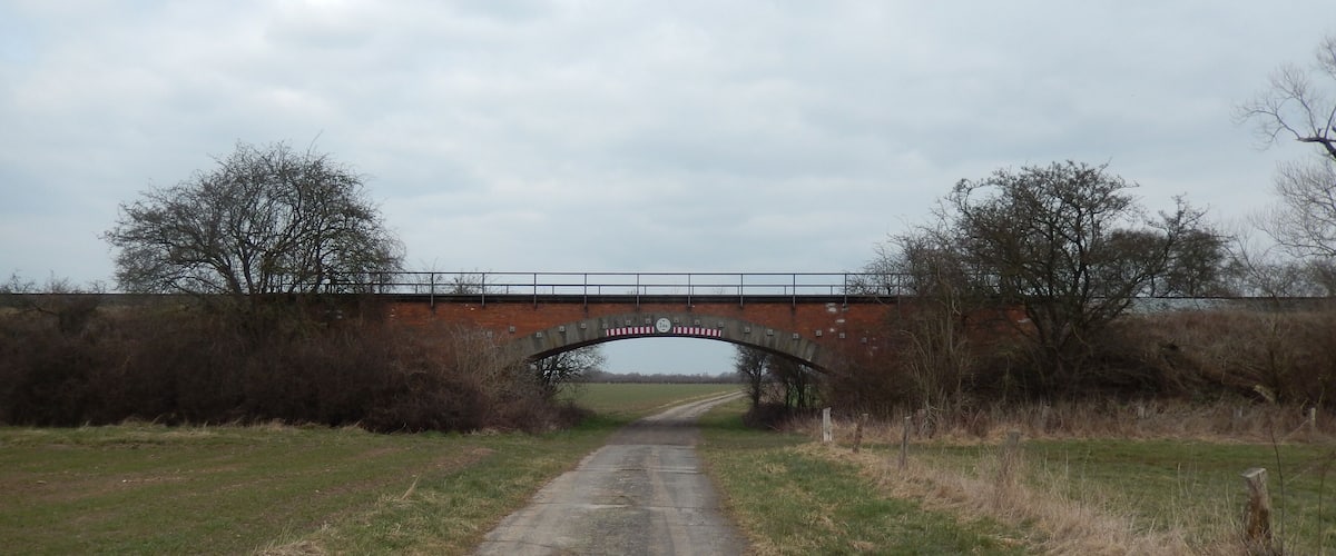 A rural road under a brick bridge with a 'no entry' sign.