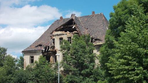Un edificio en ruinas con techumbre deteriorada y vegetación abundante.