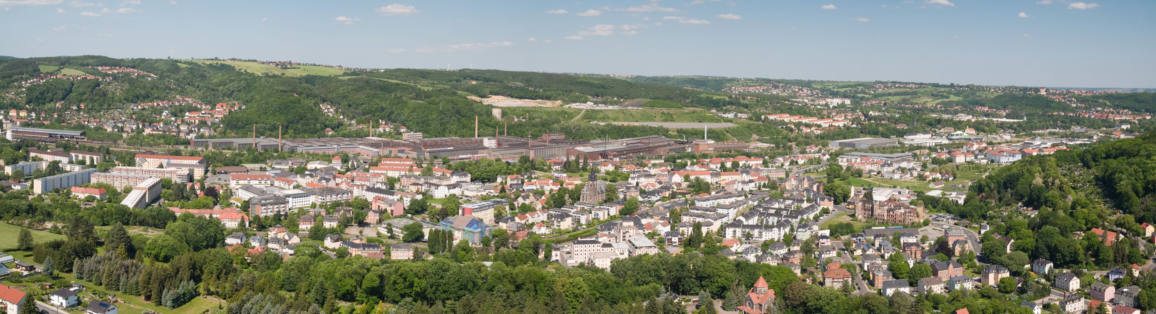 Eine Stadt mit einer Mischung aus Wohn- und Industriegebäuden, umgeben von grünen Hügeln.