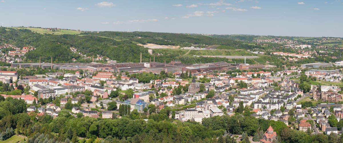 Eine Stadt mit einer Mischung aus Wohn- und Industriegebäuden, umgeben von grünen Hügeln.