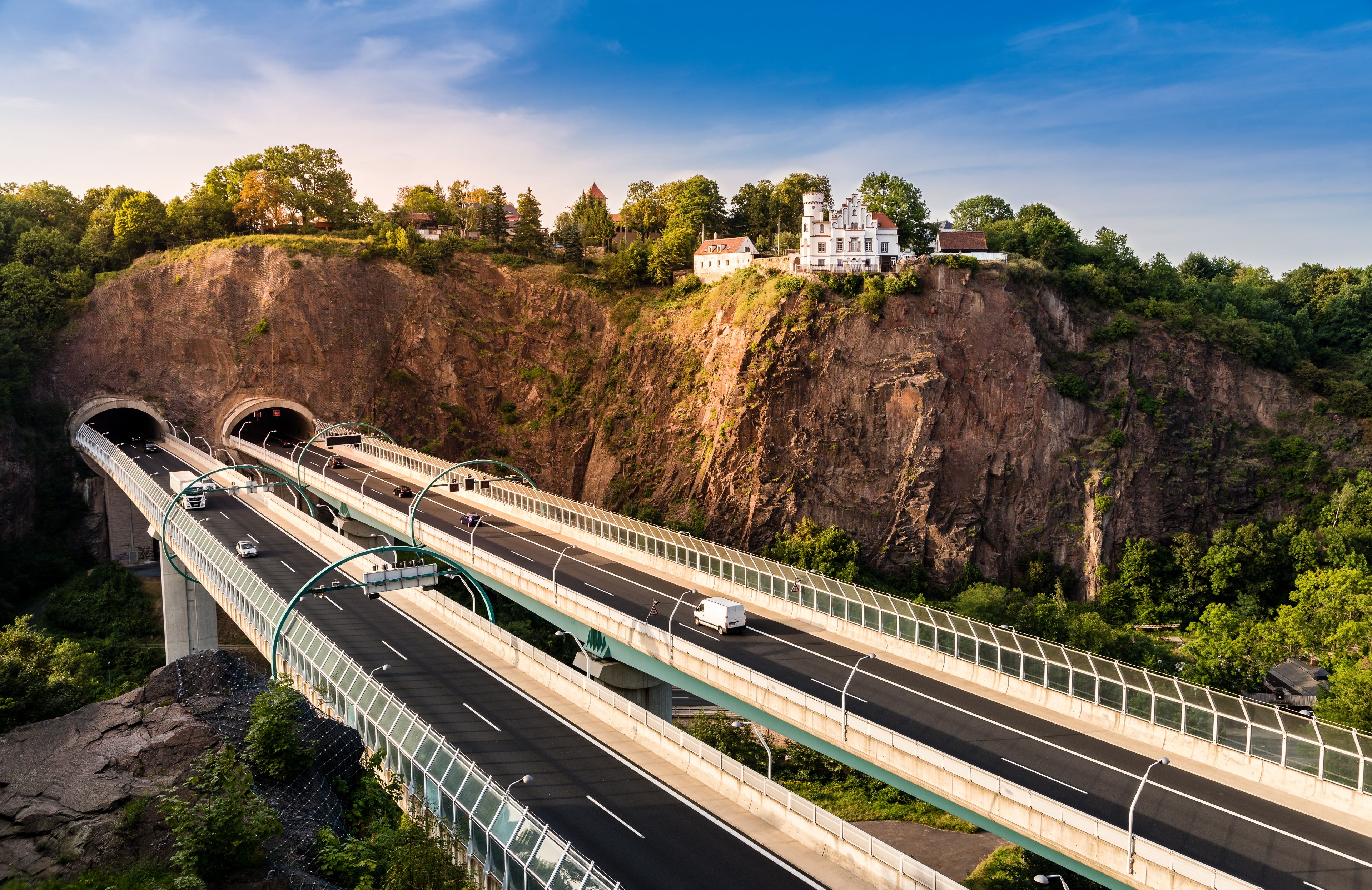 A multi-level highway bridge with vehicles, a tunnel entrance, and a castle on a cliff.