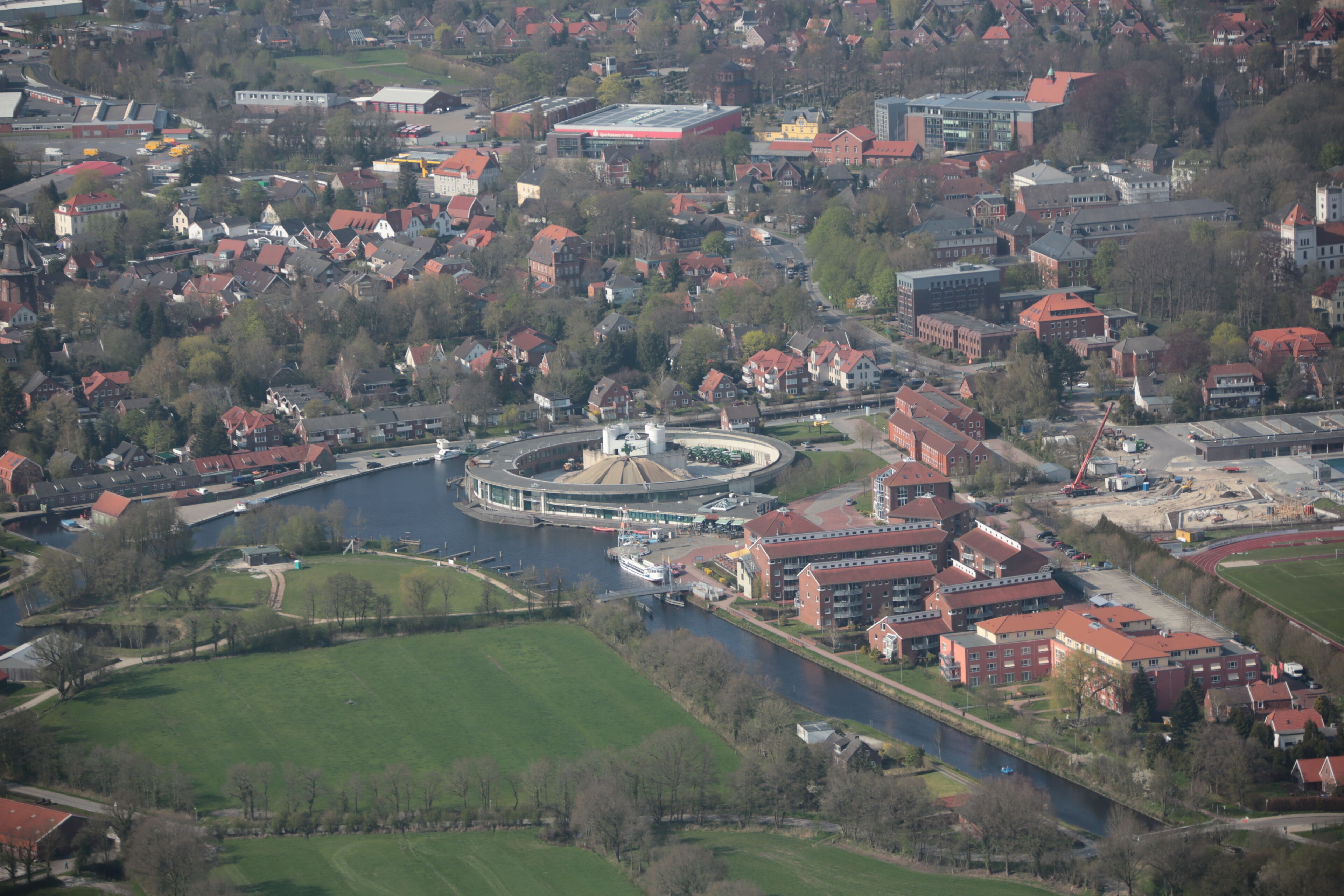 An aerial view of a town with a river, green fields, and red-roofed buildings.