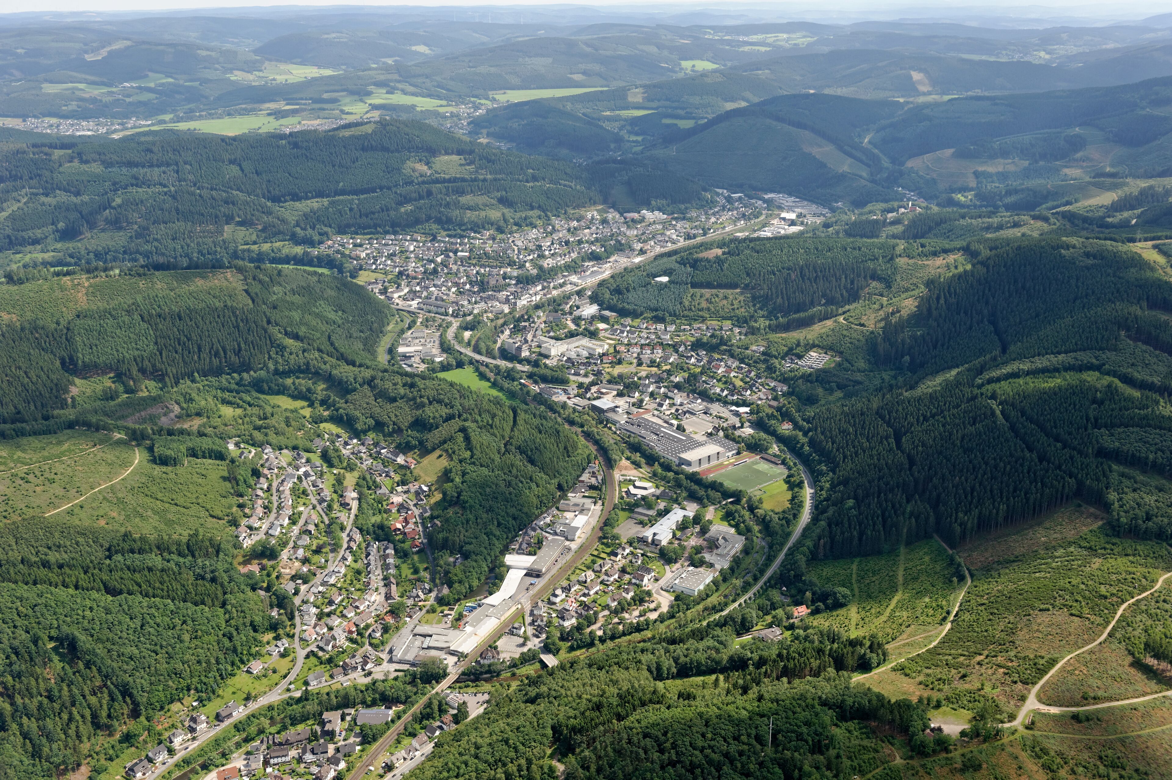 An aerial view of a town nestled in a valley with dense forests and rolling hills.