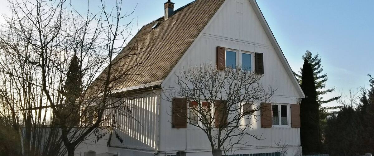A white house with a brown roof, surrounded by a blue fence and bare trees.