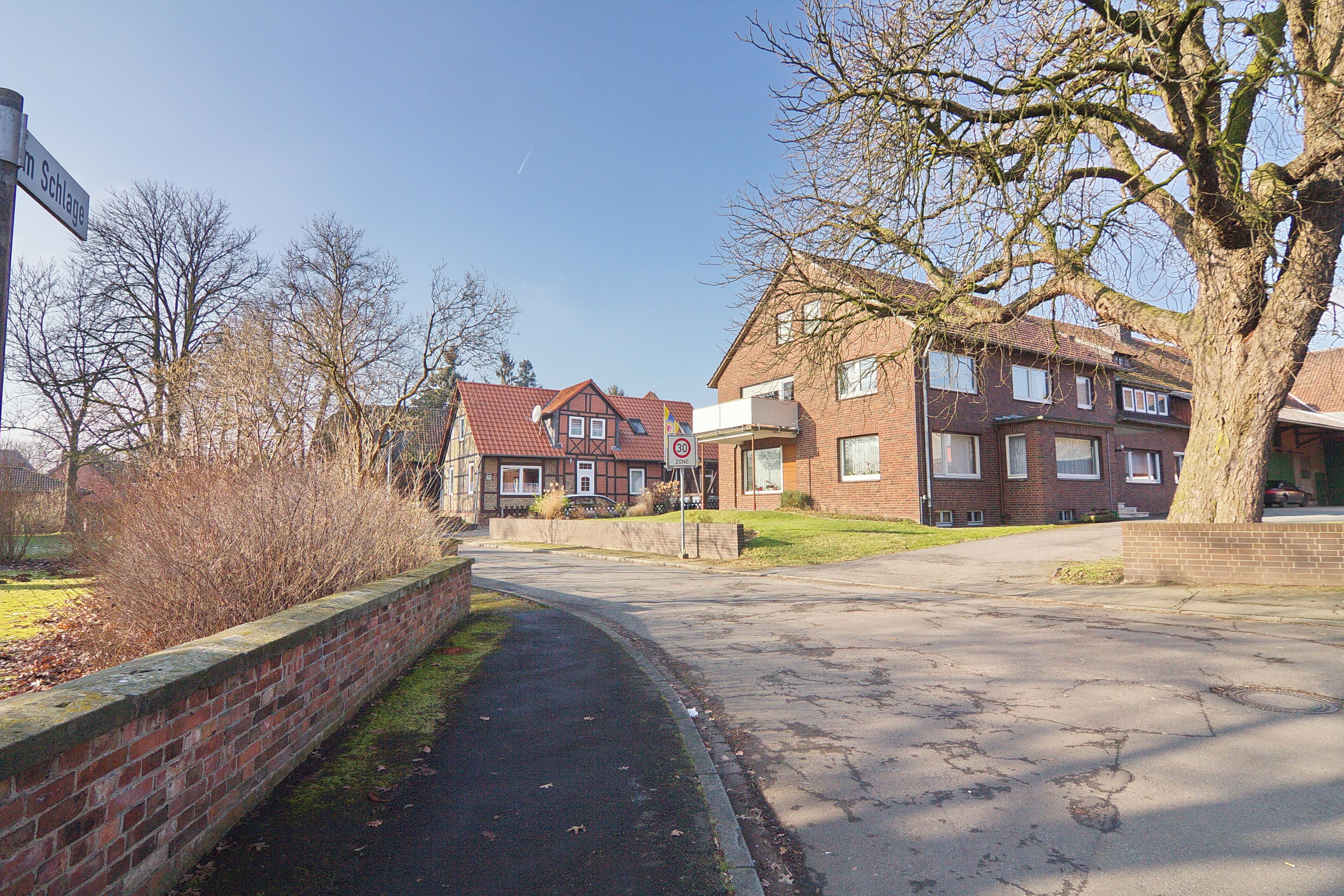 A residential street with brick houses, a paved road, and a brick wall.