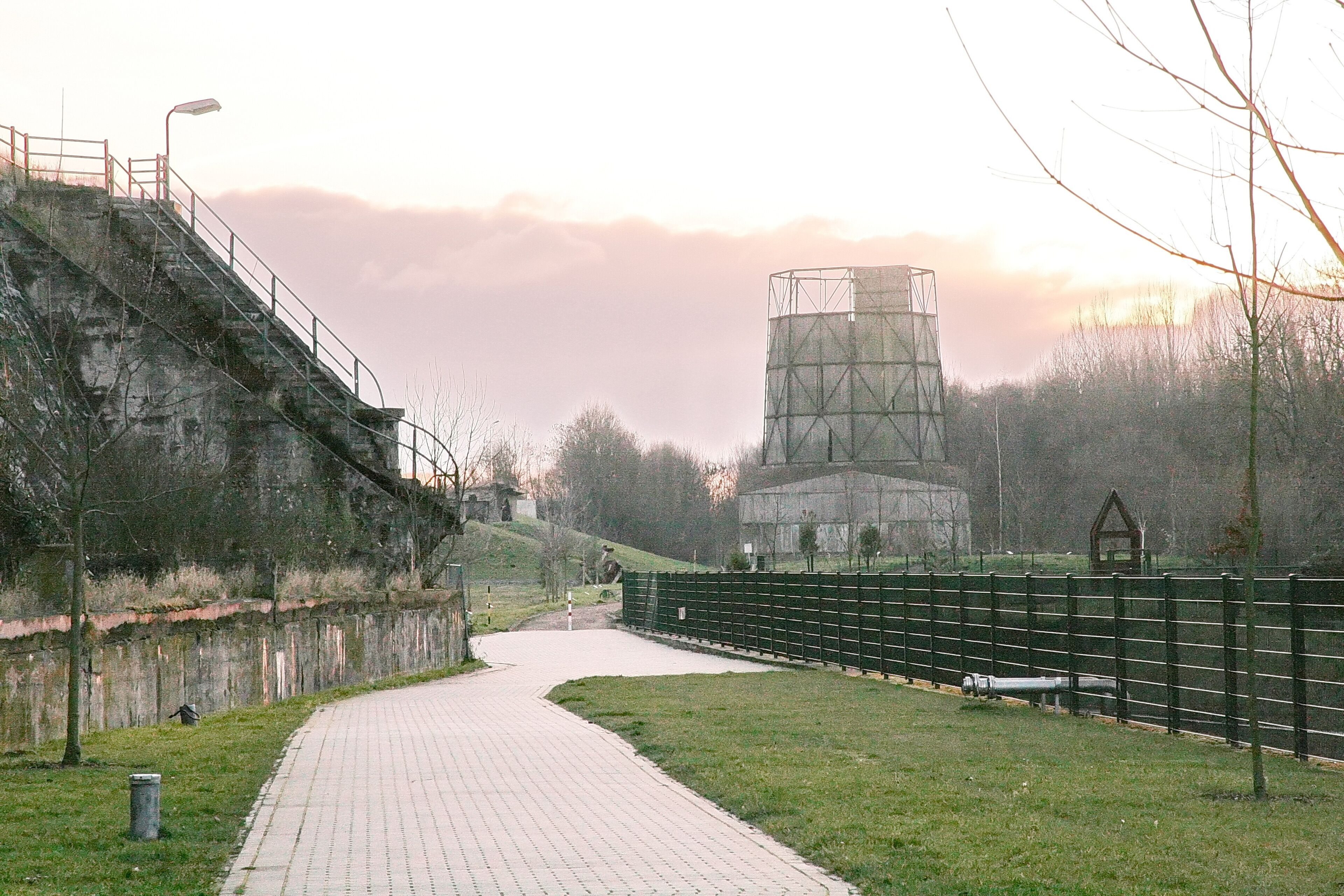 A paved pathway, a metal fence, and a large industrial structure.