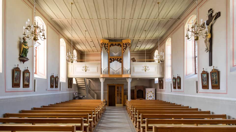 A church interior with wooden pews, a pipe organ, and religious artwork.