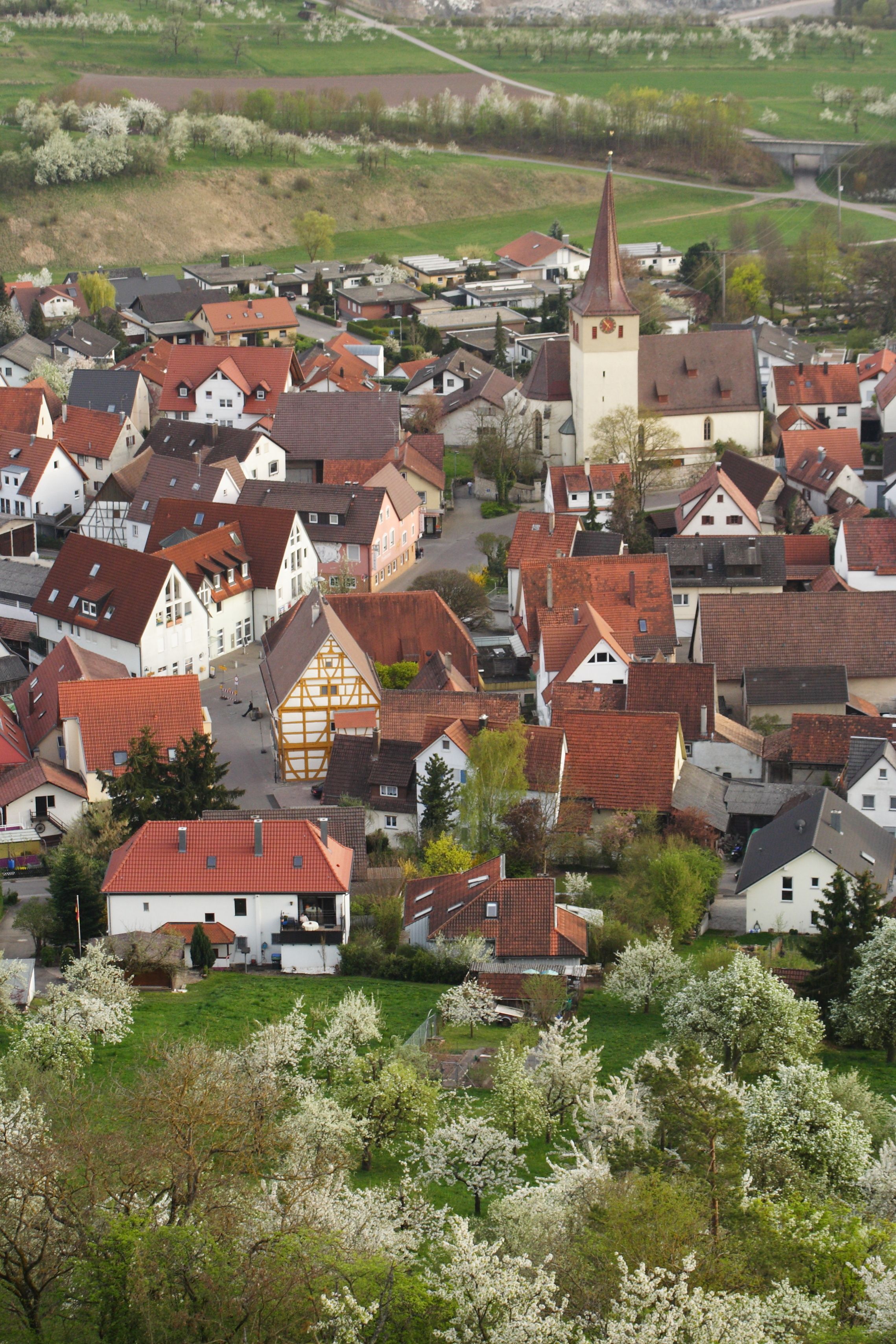 A town with traditional half-timbered houses, a church with a tall steeple, and blooming trees.