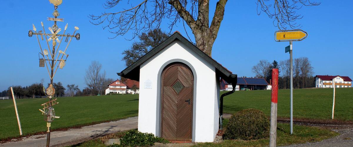 A small white chapel with a brown door, a weather vane, and a directional sign.