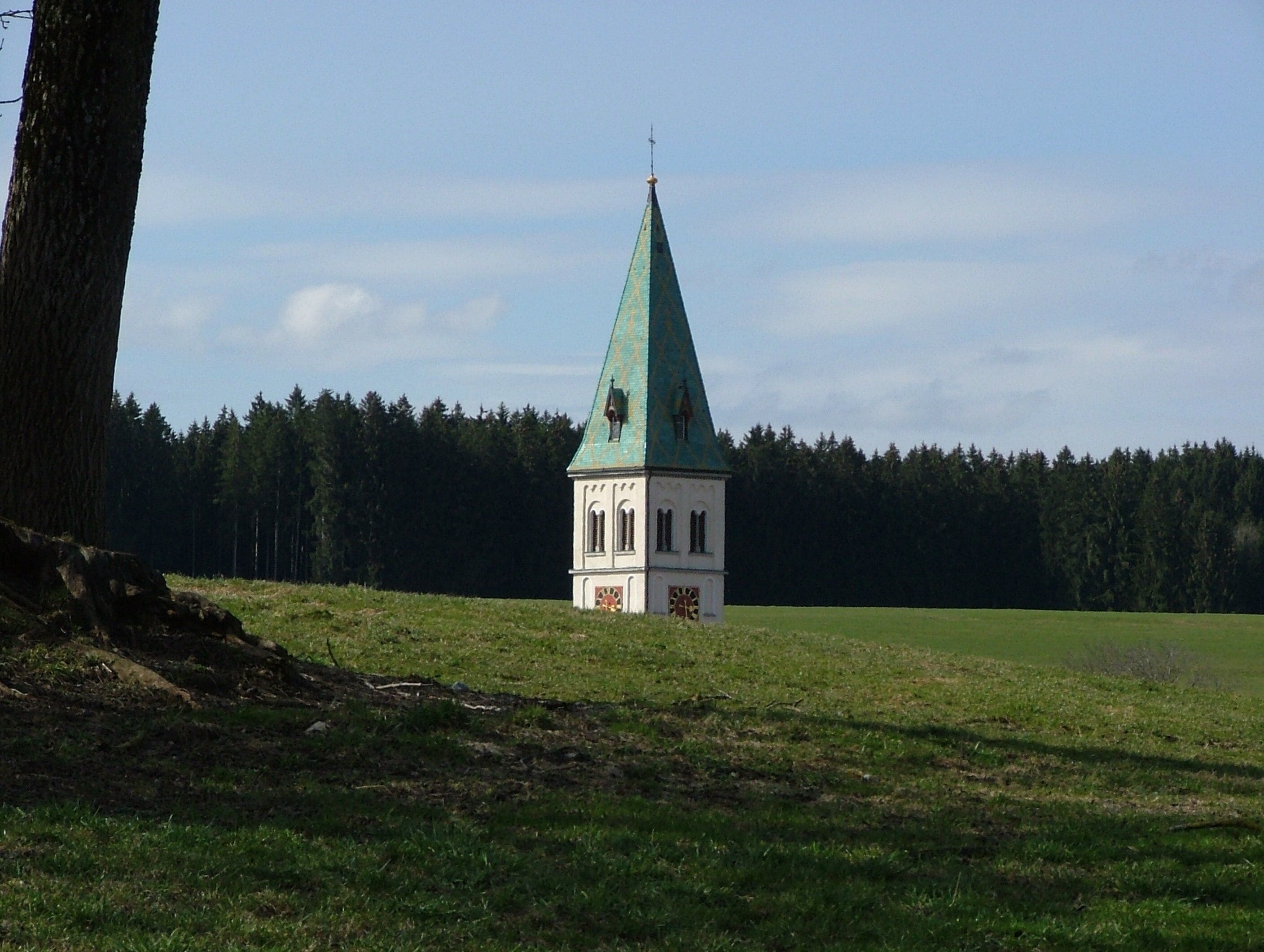 A small church with a green spire in a grassy field.
