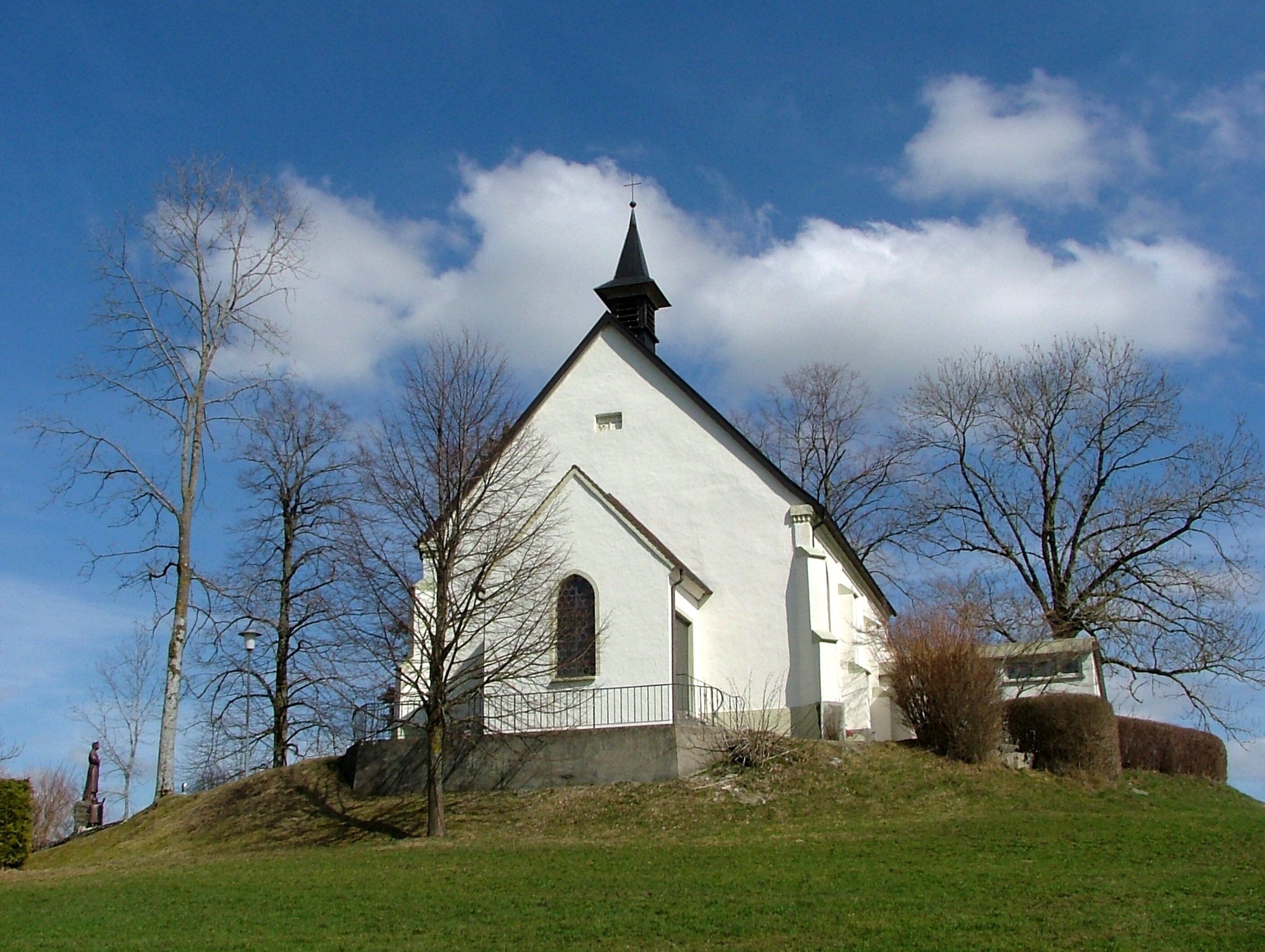 A white church with a pointed steeple on a grassy hill under a blue sky.