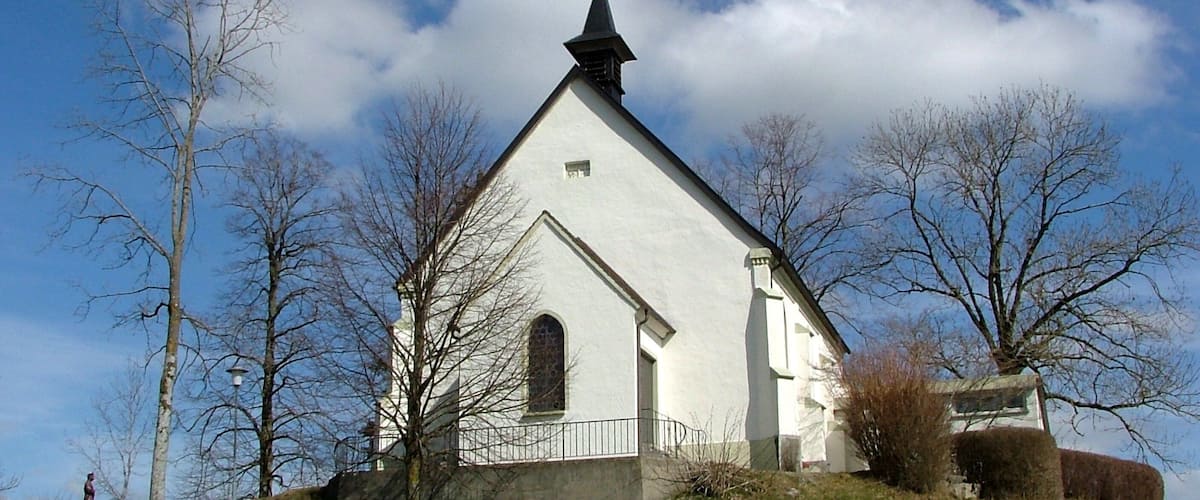 A white church with a pointed steeple on a grassy hill under a blue sky.