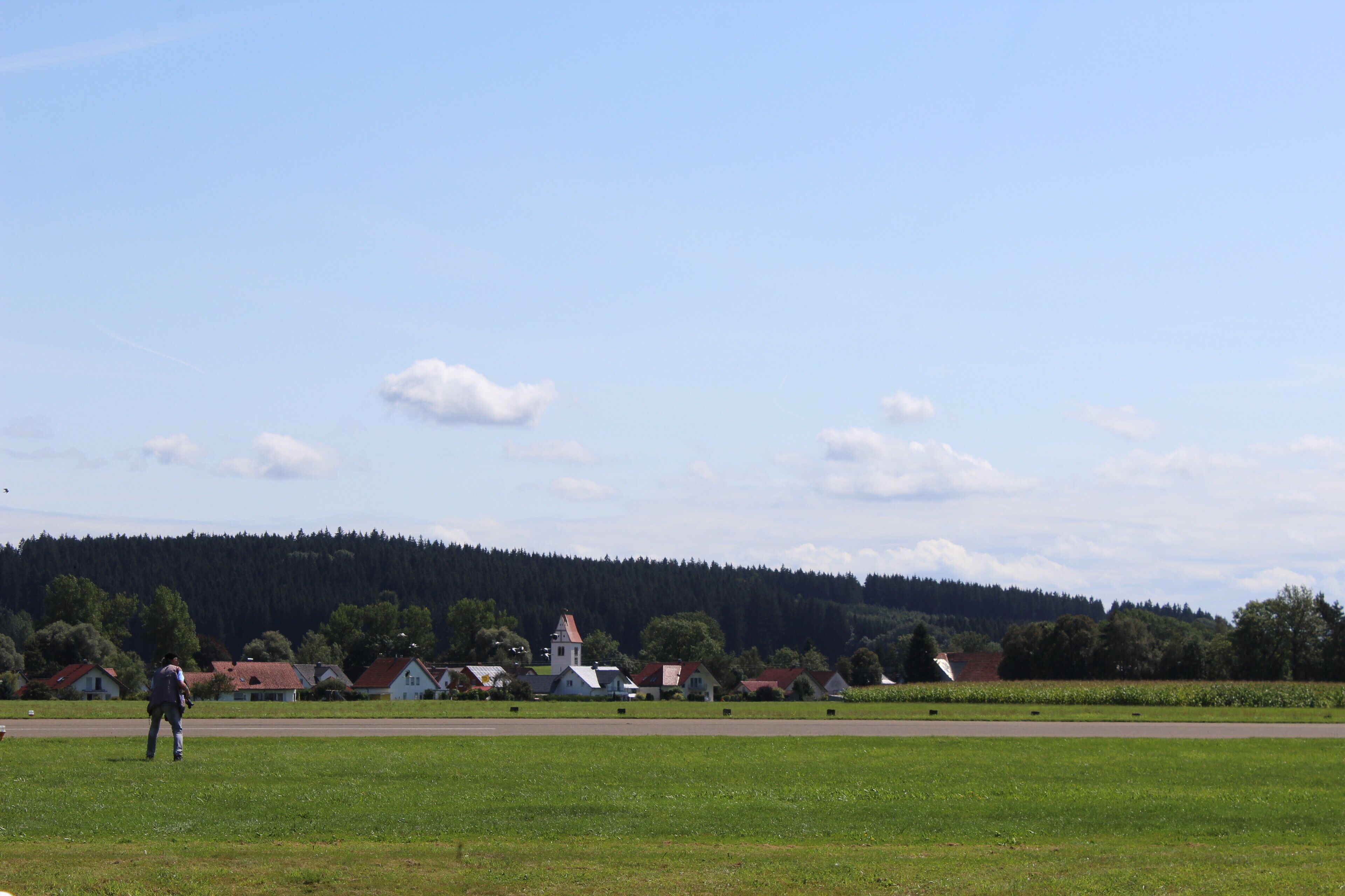 A rural landscape with a church, houses, and a forested hill in the background.