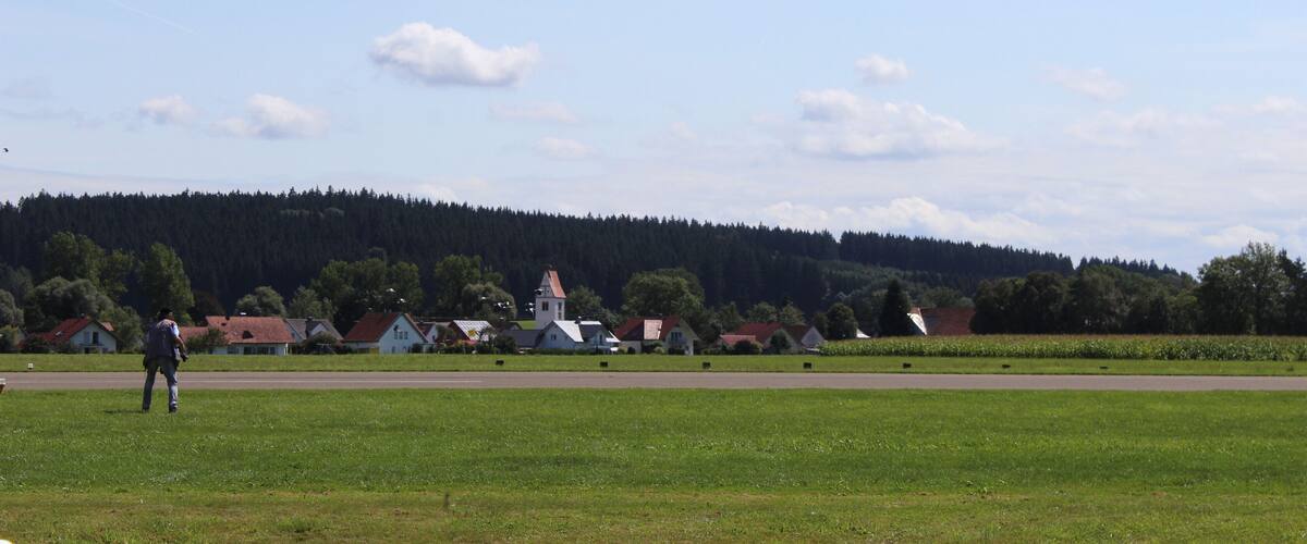 A rural landscape with a church, houses, and a forested hill in the background.
