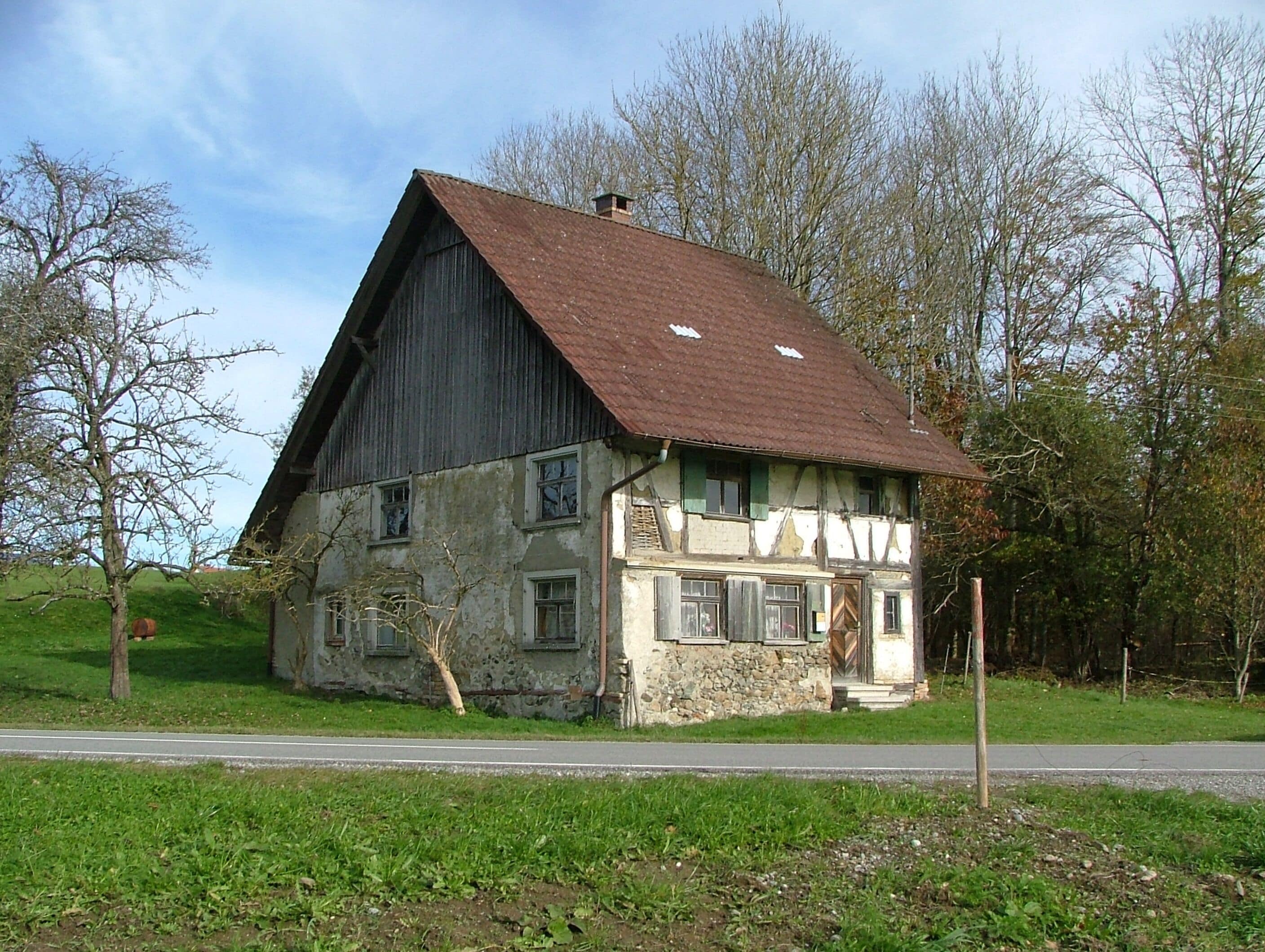 A large, two-story house with a steeply pitched roof, surrounded by trees and a grassy area.