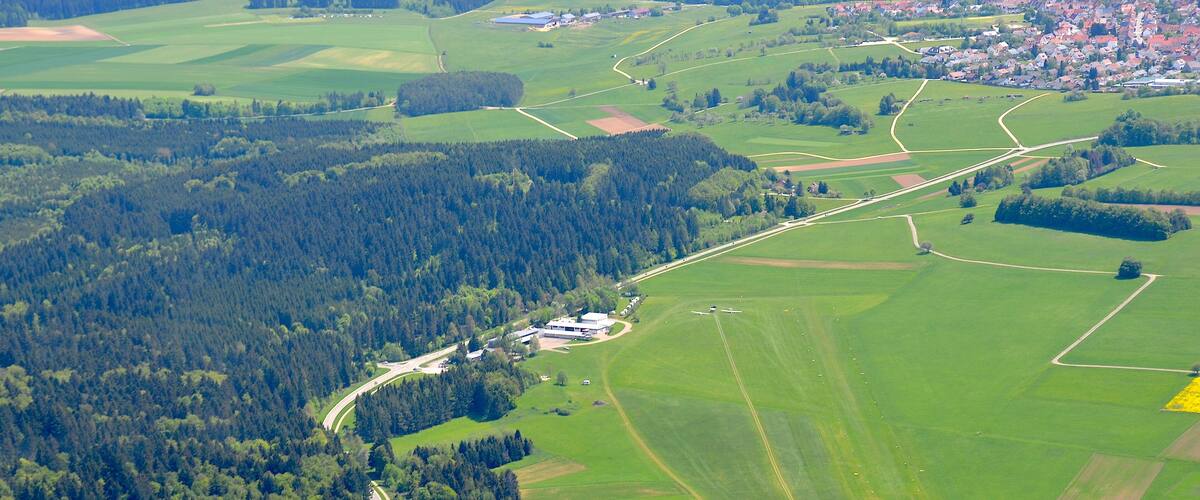 An aerial view of a rural landscape with a village, green fields, and a winding road.