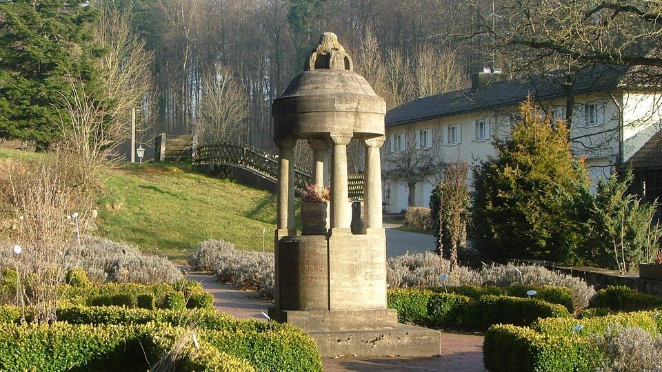 A stone gazebo in a landscaped garden with a pathway leading to a house.