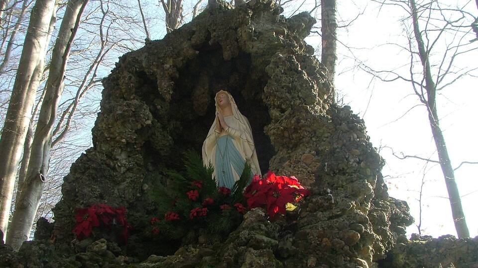 A statue of the Virgin Mary in a rocky niche surrounded by red flowers.