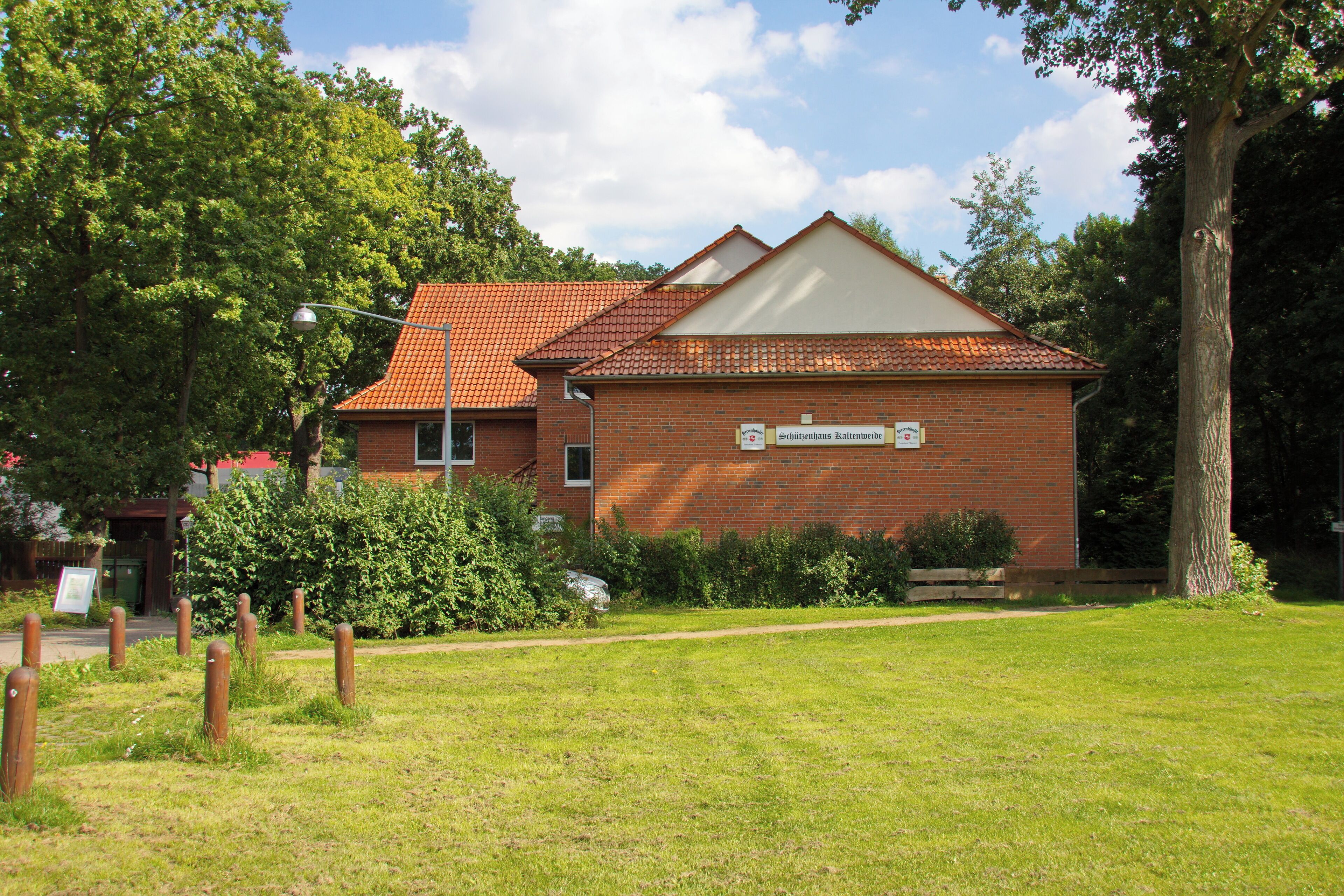 A brick building with a red-tiled roof, surrounded by a grassy area and trees.