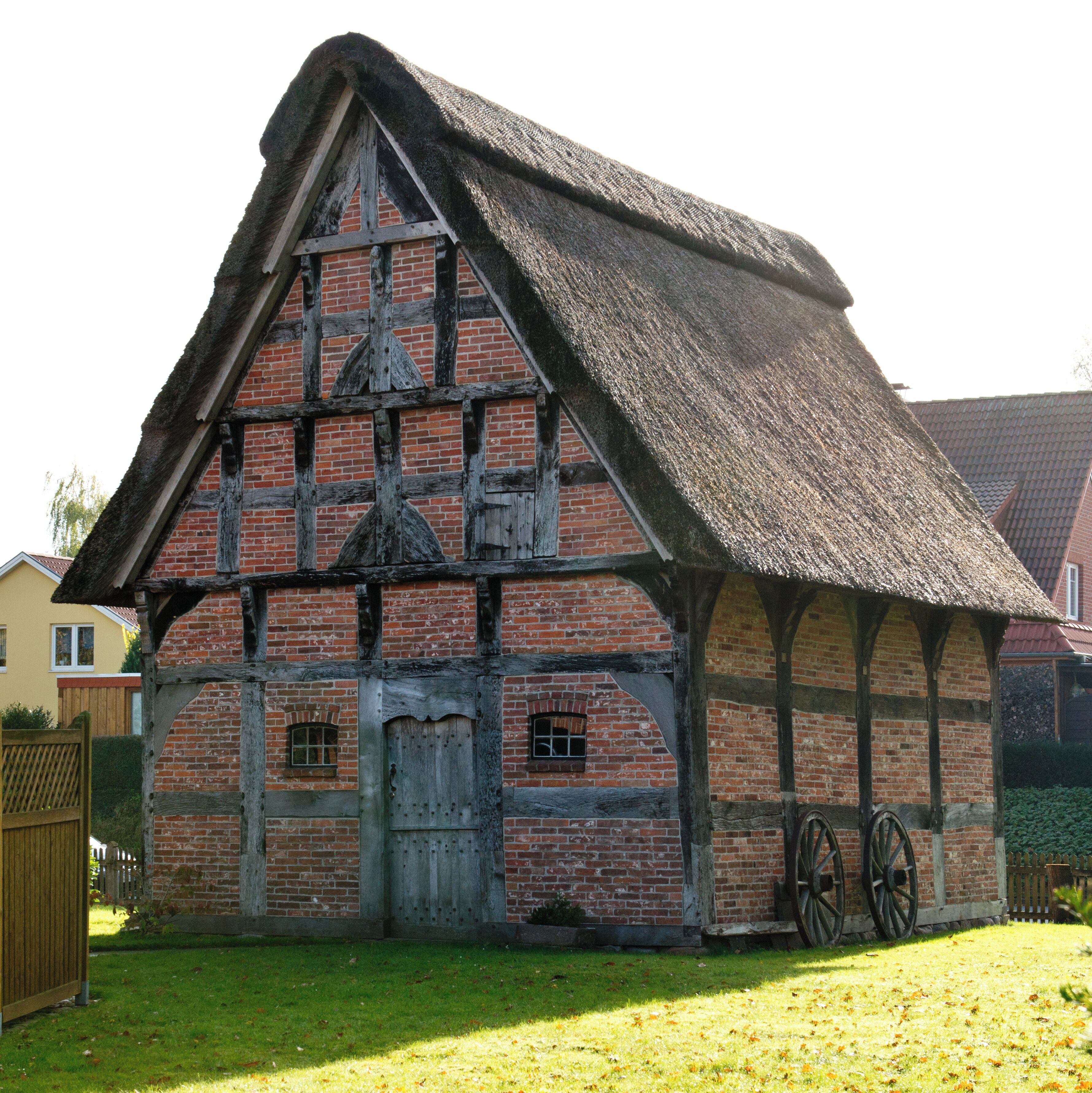 A traditional half-timbered house with a thatched roof and a wooden wheel.