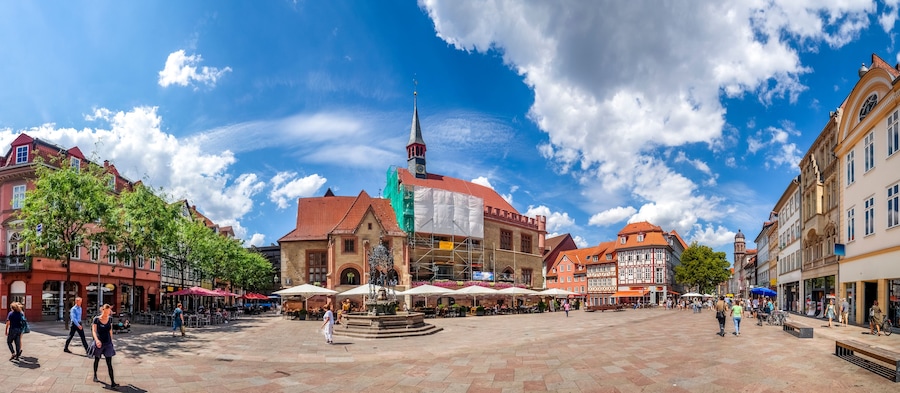 A bustling square with historic buildings, a prominent clock tower, and a fountain.