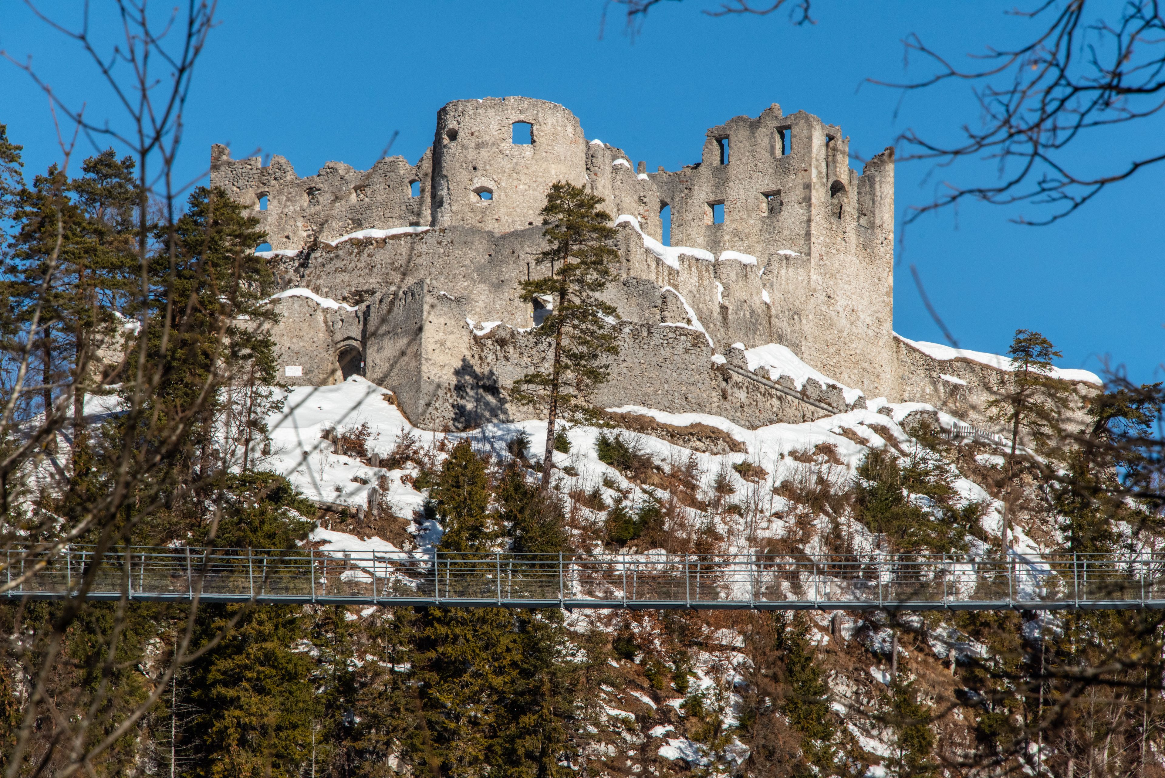 A snow-covered castle on a hill with trees in the foreground and a clear blue sky.