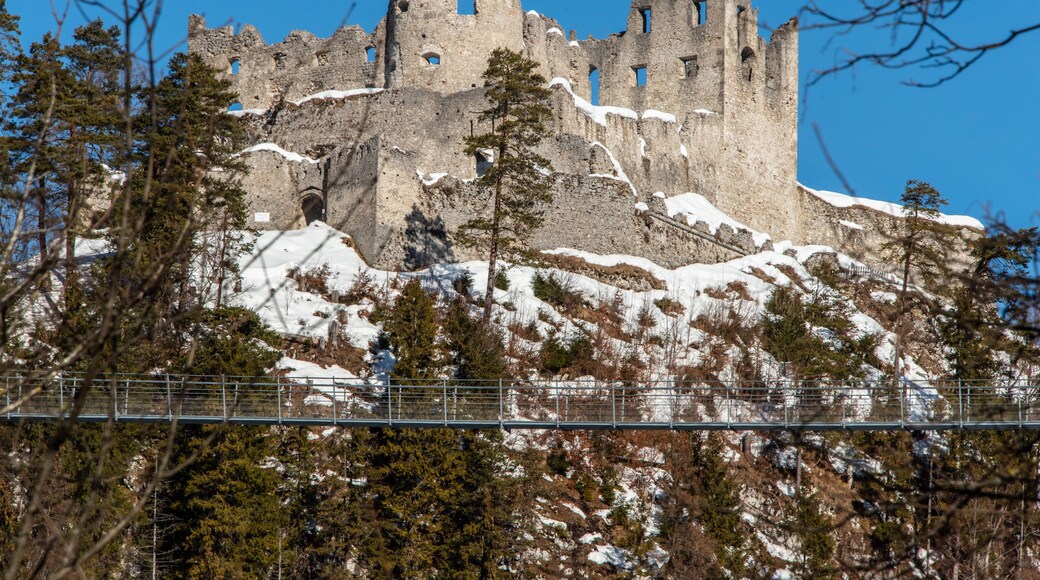 A snow-covered castle on a hill with trees in the foreground and a clear blue sky.
