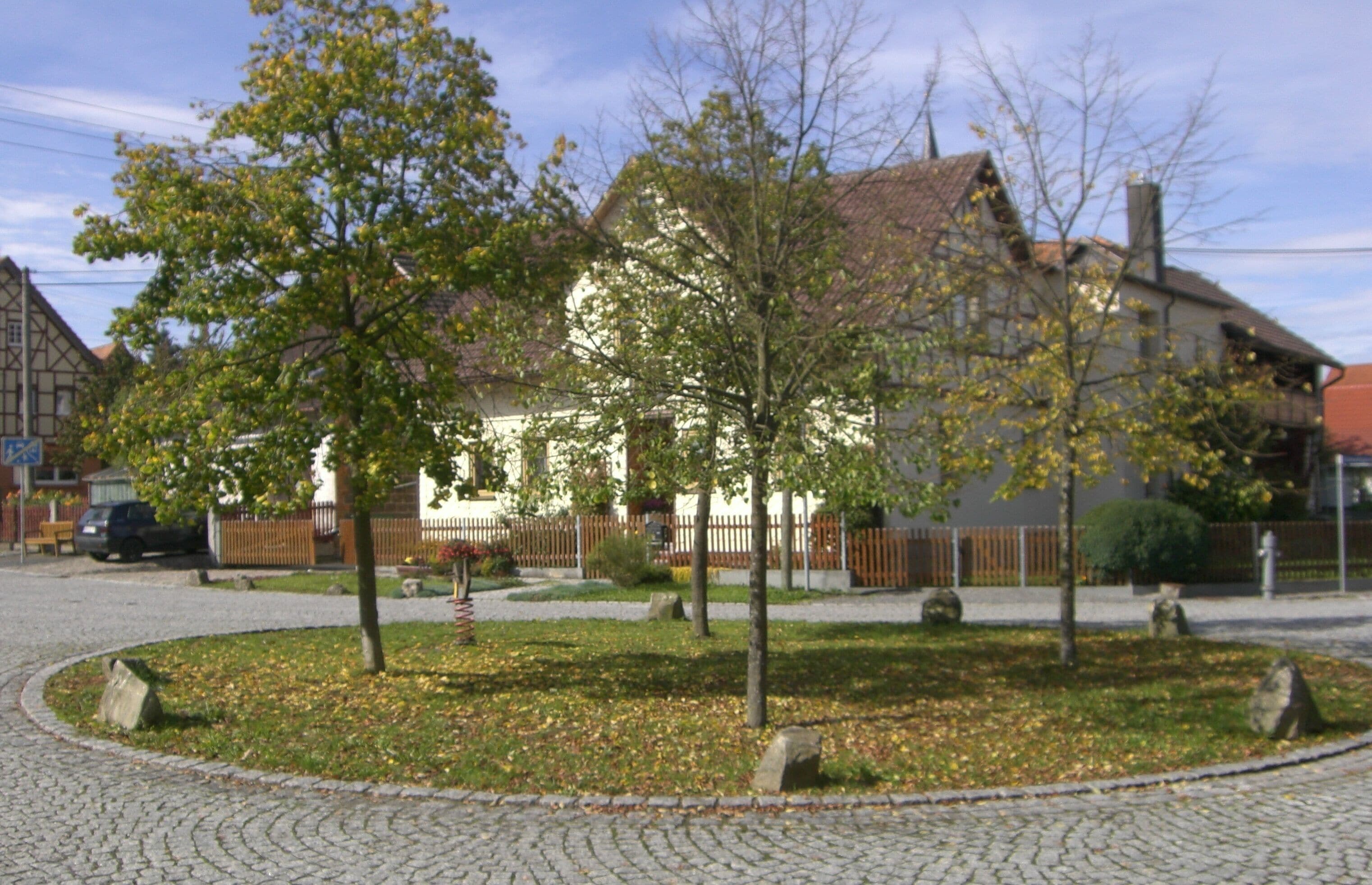 A cobblestone street with a white house, trees, and a fence.