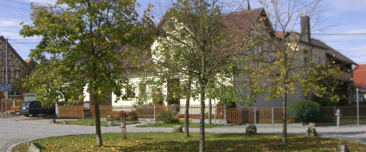A cobblestone street with a white house, trees, and a fence.