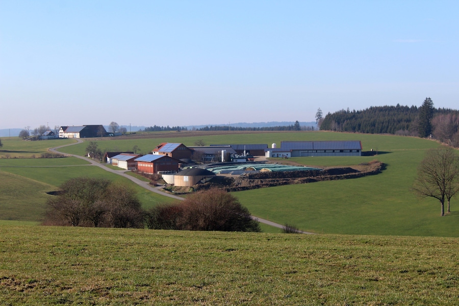 A rural landscape with green fields, a winding road, and several farm buildings.