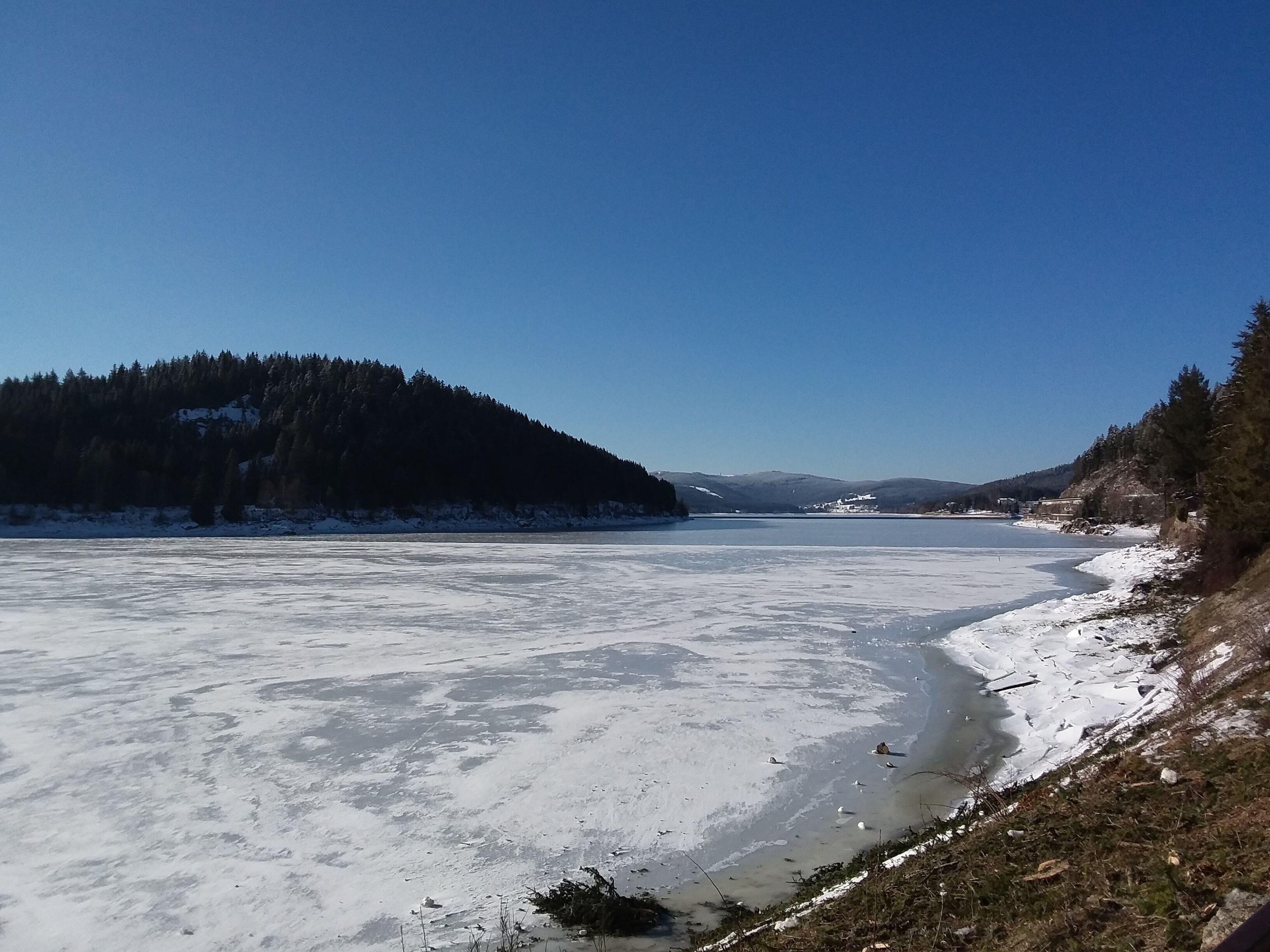 A frozen lake surrounded by snow-covered hills and dense forests.