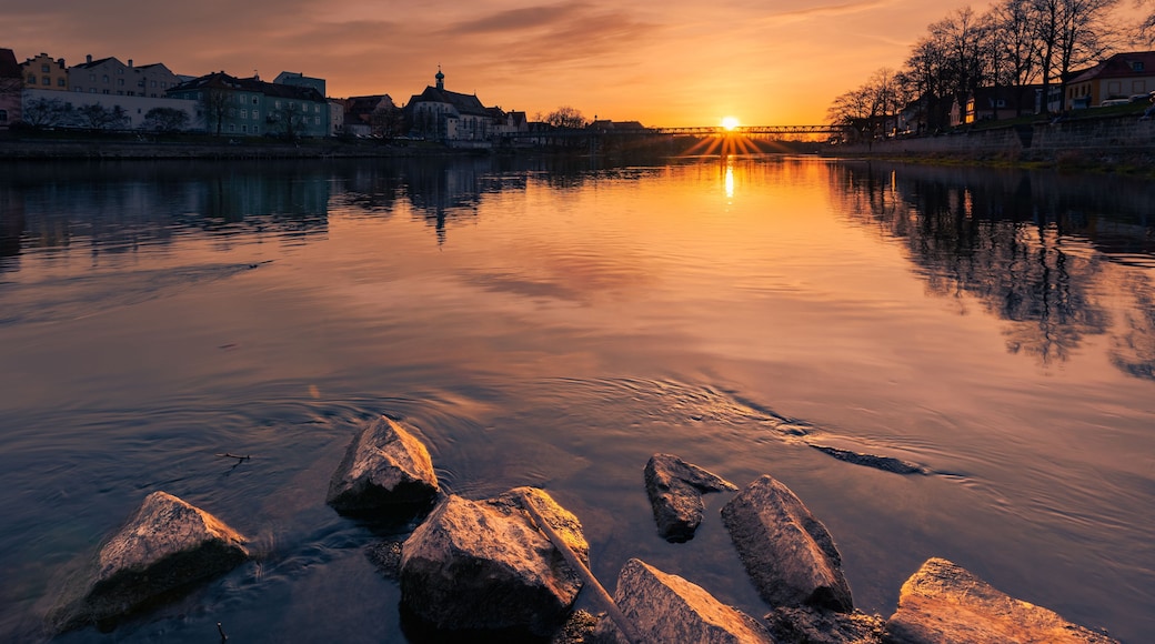 Un atardecer sobre un río tranquilo, con edificios a la otra orilla y un puente en la distancia.