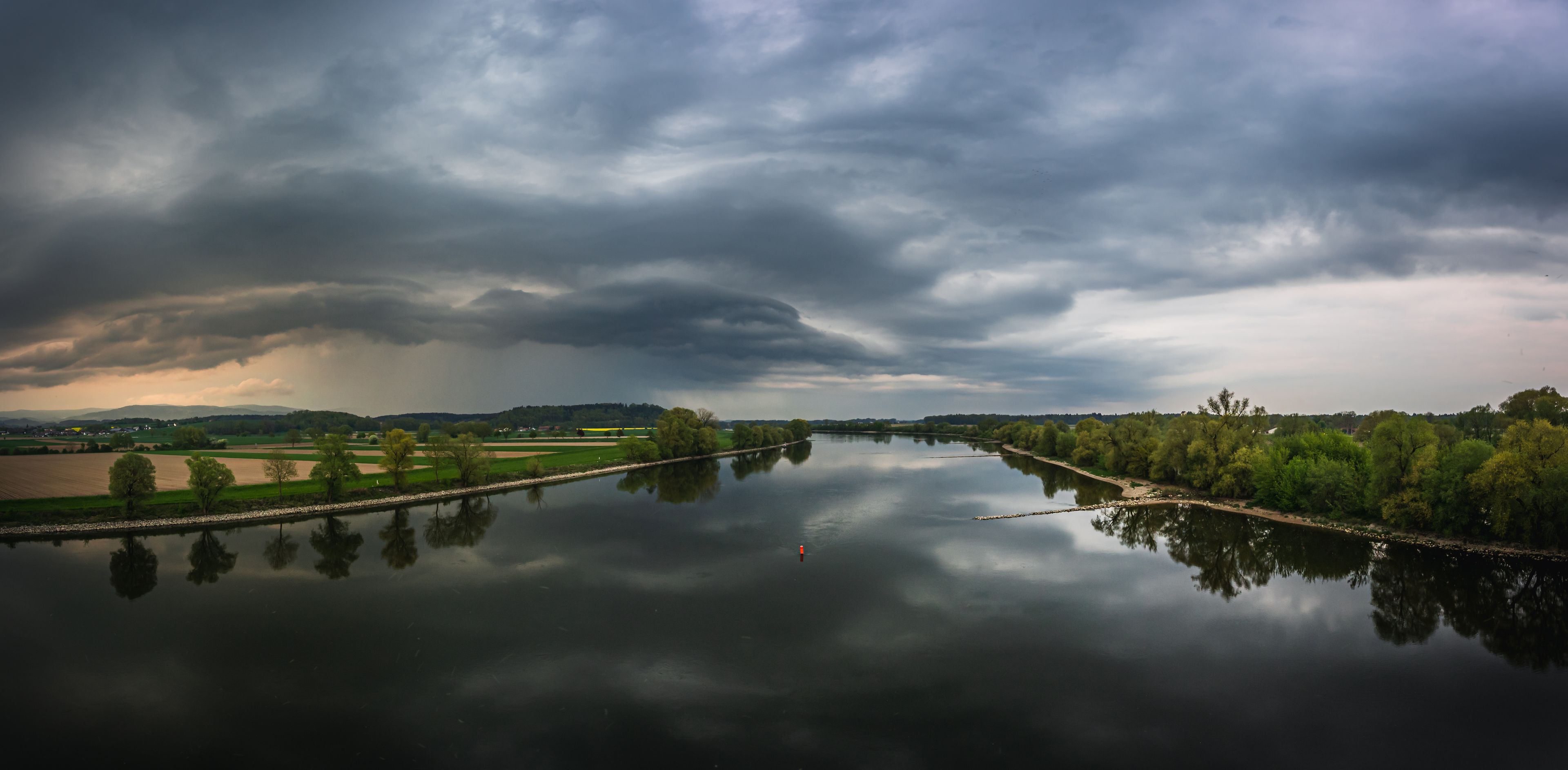 Un río que refleja cielos nublados, rodeado de campos y árboles.