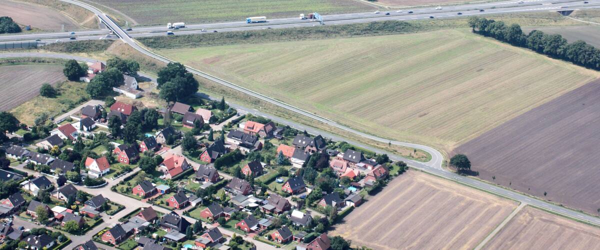 An aerial view of a rural area with a highway, fields, and a residential area with red-roofed houses.